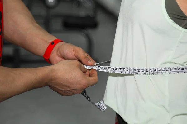 パーソナルトレーナー 栄養士 フィットネス 動機づけ 健康的なライフスタイル 男は測定テープで女の子の腰を測定します 閉じて マクロ写真 訓練の準備 — ストック写真