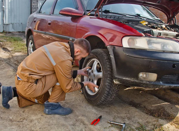 A mechanic removes a car tire. A man working on a machine to remove rubber from a wheel disk