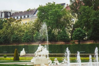 Viyana, Avusturya - 11, 05, 2019: Bulutlu bir yaz günü. Belvedere bahçeleri, gölleri, perileri ve arka planda Belvedere sarayı olan imparatorluk barok parkı. Yeşillik arkaplanındaki çeşmeler