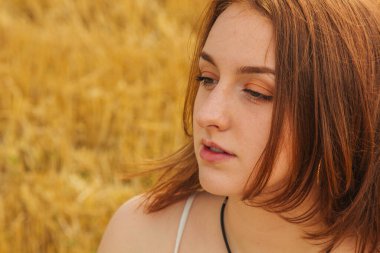 Buğday tarlasının ortasında güzel bir kızıl saçlı kızın portresi. Çerçeveye bakıyor, kahverengi gözlü. Rüzgarlı saçlarla oynuyor. Beyaz pamuklu elbise, eko tarzı.