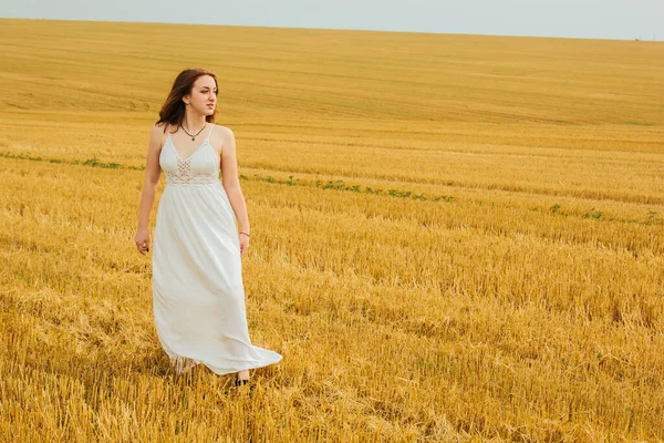 Good outdoor recreation. Young beautiful redhead woman in the middle of a wheat field, having fun. Summer landscape, good weather. Windy day with the sun and clouds. White cotton dress, eco style