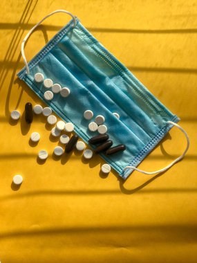 Vitaminler ve doktor maskesi, sarı arka planda Corona virüsü koruma konsepti. Solunum maskesi ve haplar. Coronavirus, hastane veya çevre kirliliği yüz maskelemeyi korur