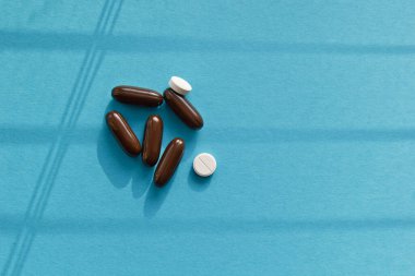 Vitaminler ve doktor maskesi, mavi arka planda taç virüsü koruma konsepti. Güneşten gelen gölgeler. Solunum maskesi ve haplar. Coronavirus, hastane veya çevre kirliliği yüzleri korur