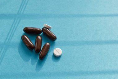 Vitaminler ve doktor maskesi, mavi arka planda taç virüsü koruma konsepti. Güneşten gelen gölgeler. Solunum maskesi ve haplar. Coronavirus, hastane veya çevre kirliliği yüzleri korur