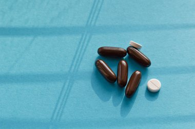 Vitaminler ve doktor maskesi, mavi arka planda taç virüsü koruma konsepti. Güneşten gelen gölgeler. Solunum maskesi ve haplar. Coronavirus, hastane veya çevre kirliliği yüzleri korur