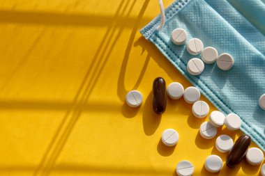 Vitaminler ve doktor maskesi, sarı arka planda Corona virüsü koruma konsepti. Solunum maskesi ve haplar. Coronavirus, hastane veya çevre kirliliği yüz maskelemeyi korur