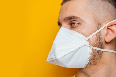 Corona virüsü. Sarı arka planda solunum cihazındaki genç adam. Ağız ve gözlerin virüslerden, enfeksiyonlardan ve egzoz dumanından korunması. Enfeksiyonu önleme yöntemleri