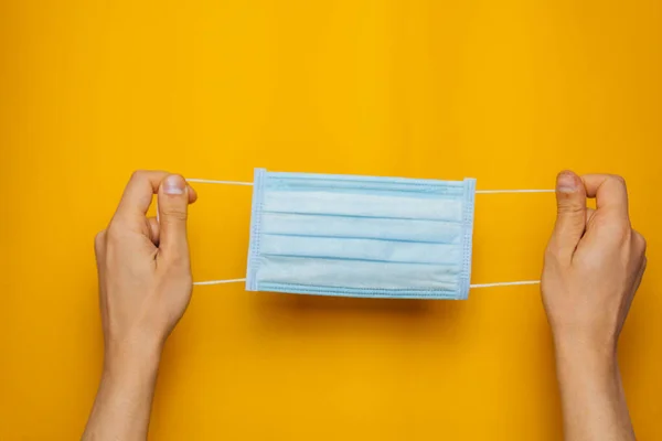 Mask to protect the respiratory tract in the hands on an orange background. Methods of prevention of protection against the virus. Place for text