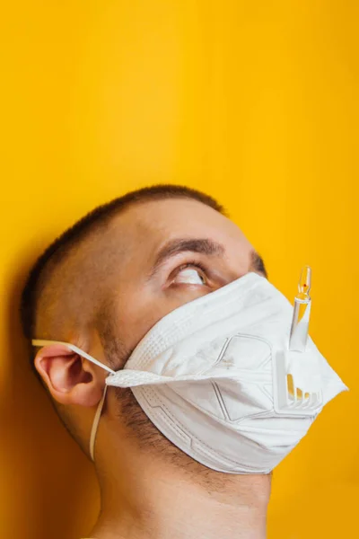 stock image Portrait of a young doctor in a respirator on a yellow background. Respiratory coronavirus vaccine ampoules. A look at the ampoule. The inventor of the drug. The concept of a long illness