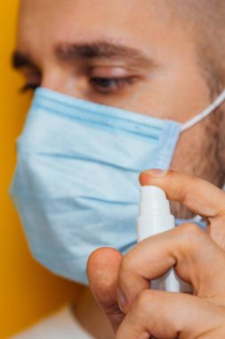 Sarı arka planda maskeli bir gencin portresi. Ellerini antiseptikle dezenfekte ediyor. Böcek ilaçlama. Coronavirus konsepti. Mikrop ve virüslere karşı koruma