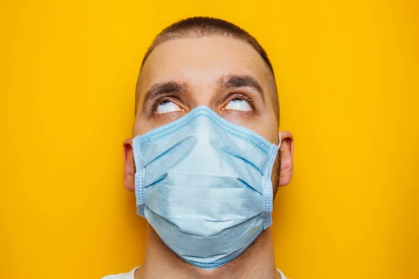 Closeup portrait of an attractive young man rolled his eyes in a protective mask on his face. Fear of getting sick, coronavirus concept. Without pupils