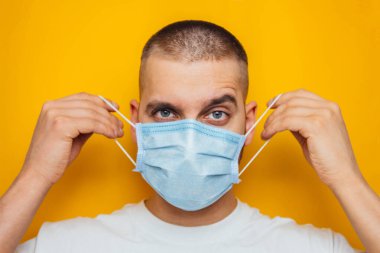 Genç bir adam tıbbi maske takıyor. Sarı zemin üzerinde nezle ve grip virüslerinin önlenmesi. Stüdyo fotoğrafı. Coronavirus ve covid-19 konsepti