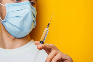 Sarı arka planda solunum cihazındaki genç bir adamın portresi. Koronavirüs aşısıyla ampul tutuyormuş. Soğuk algınlığı ilacı. Koronavirüs konsepti