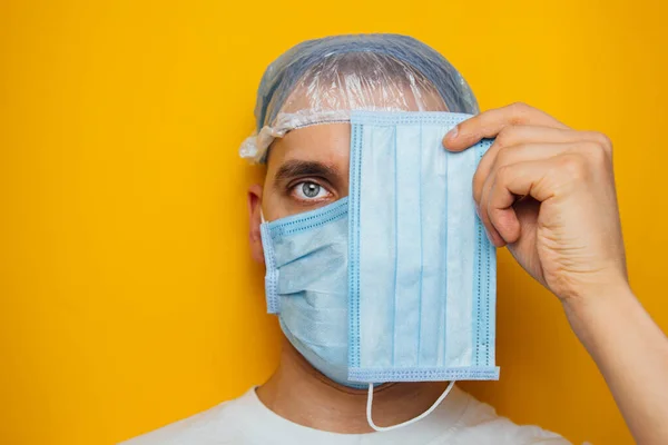 The guy puts on a respiratory mask over his eyes. Attractive man puts on a mask and looks at the camera. Colds, flu, virus, tonsillitis, acute respiratory infections, quarantine, epidemic concept