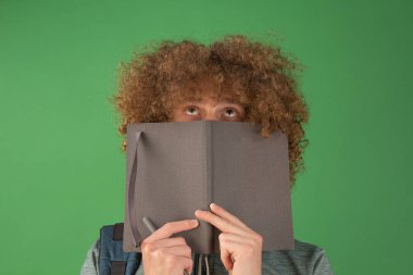 Dizüstü bilgisayarı olan genç bir adam çevrimiçi eğitimle meşgul. Kıvırcık saçlı yakışıklı bir adam elinde açık bir defter tutuyor ve üzerinde çalışıyor. Bilgi, teknoloji konsepti. Karantina