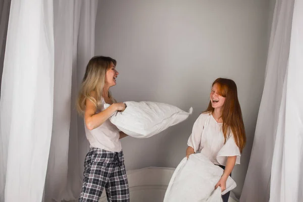 Family having funny pillow fight on bed. Beautiful mom with her little cute daughter spending free time together