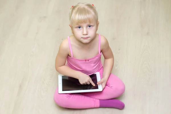 Маленькая девочка в розовом платье смотрит вверх и нажимает на планшет Лицензионные Стоковые Изображения