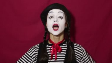 Güzel pandomimci kız başını olumlu bir şekilde sallar ve kameraya bakarken evet der. Çizgili tişörtlü güzel pandomimci kız başını olumlu bir şekilde sallıyor ve gülümsüyor. Kırmızı arkaplanda bir portre.