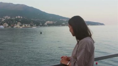 Mavi deniz ve dağların arka planında güzel bir kızın portresi. Deniz ve plajların arka planında çekici bir kızın yakın plan portresi. Kameraya bakıyor, gülümsüyor ve elini sallıyor..