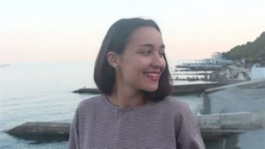 Mavi denizin arka planında güzel bir kızın portresi. Deniz ve plajların arka planında çekici bir kızın yakın plan portresi. Kameraya bakıyor, gülümsüyor ve elini selamlıyor..