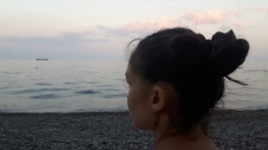 Denizin arka planında çekici bir kızın yakın plan portresi, kameraya bakıyor ve gülümsüyor. Mavi denizin arka planında genç güzel bir kızın portresi..
