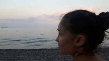Denizin arka planında çekici bir kızın yakın plan portresi, kameraya bakıyor ve gülümsüyor. Mavi denizin arka planında genç güzel bir kızın portresi..