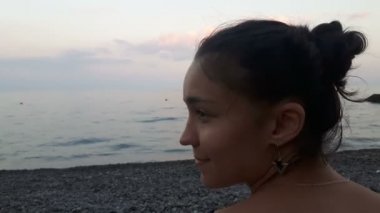 Denizin arka planında çekici bir kızın yakın plan portresi, kameraya bakıyor ve gülümsüyor. Mavi denizin arka planında genç güzel bir kızın portresi..