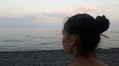 Denizin arka planında çekici bir kızın yakın plan portresi, kameraya bakıyor ve gülümsüyor. Mavi denizin arka planında genç güzel bir kızın portresi..