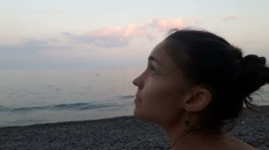 Denizin arka planında çekici bir kızın yakın plan portresi, kameraya bakıyor ve gülümsüyor. Mavi denizin arka planında genç güzel bir kızın portresi..
