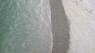 Deniz ve kayalık kıyı manzarası, deniz çakıl taşları ile. Berrak mavi suyla deniz. Kayalık sahilde deniz sörfü.