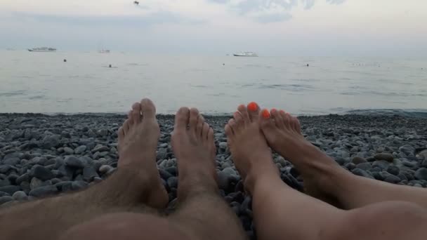 看着一个年轻小伙子和一个女孩的腿躺在蓝色的海面上 可爱的年轻夫妇躺在海滨 一对年轻夫妇在蔚蓝的大海和多云的天空中坠入爱河 — 图库视频影像