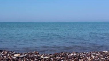 Deniz ve kayalık kıyı manzarası, deniz çakıl taşları ile. Berrak mavi suyla deniz. Kayalık sahilde deniz sörfü.