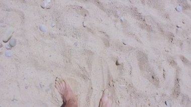 Erkek ayakları kumlu plaj boyunca yürümek. Bir adam kumlu plajda dinlenmekten hoşlanır. Bir adam denizin yanında kumda yürüyor..