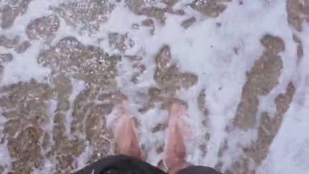Чоловічі ноги ходять по березі моря. Самець насолоджується морськими хвилями на гальковому пляжі. Чоловік насолоджується відпочинком на гальковому пляжі. Чоловічі ноги омиваються морською хвилею. — стокове відео