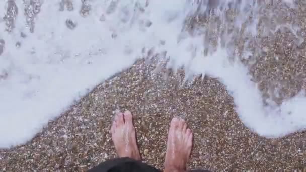 Os pés masculinos caminham ao longo da marquia.O macho aprecia as ondas do mar em uma praia de seixos. Um homem gosta de relaxar em uma praia de seixos. pés masculinos lavados por uma onda do mar . — Vídeo de Stock