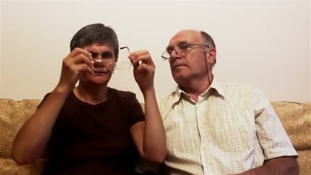 迷人的成年女子和成年男子戴眼镜试眼 一对老夫妇坐在家里的沙发上 戴上眼镜 互相商量着 — 图库视频影像