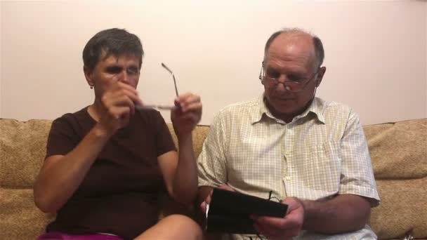高齢者のカップルは 自宅でソファに座って 視力のための眼鏡を試して お互いに相談してください — ストック動画