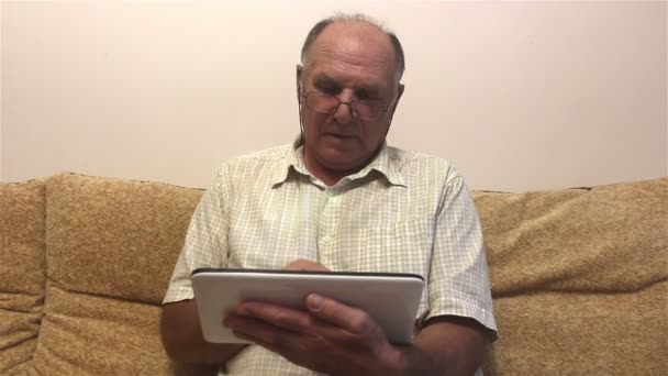 Starszy Mężczyzna Pracuje Tablecie Siedząc Kanapie Domu Atrakcyjny Staruszek Okularach — Wideo stockowe