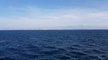 Okyanus manzarası ve gökyüzündeki bulutlar. Okyanus üzerinde güneşli havada bulutlu mavi gökyüzü. Ufuktaki dağlar ve okyanus.