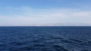 Okyanus manzarası ve gökyüzündeki bulutlar. Okyanus üzerinde güneşli havada bulutlu mavi gökyüzü. Ufuktaki dağlar ve okyanus.