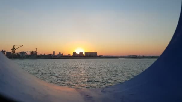 海洋和海港的日落 透过船的港口欣赏日落和海洋 从邮轮的客舱到海洋和城市的视野 — 图库视频影像