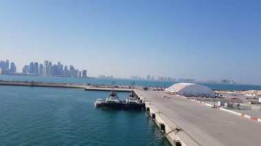 Ufukta gökdelenler ile deniz limanı ve şehir görünümü. Demirli gemilerle deniz limanı. Mavi gökyüzünün arka planındaki gökdelenler.