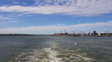 Güneşli havada gemiyi takip eden dalgaların görüntüsü. Martılar geminin arkasında uçar. Geminin kıç tarafından kıyı ve okyanus manzarası.