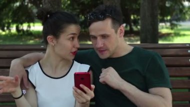 Genç, güzel bir kız ve yakışıklı genç erkek arkadaşı, parkta otururken sosyal ağda haberleri akıllı telefonlarından izliyorlar. Gülümsüyorlar ve haberleri tartışıyorlar..