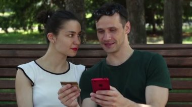 Birbirine aşık genç bir çift, parktaki bankta otururken internetten satın aldıklarını ödemek için kredi kartı bilgilerini akıllı telefona aktarıyor..