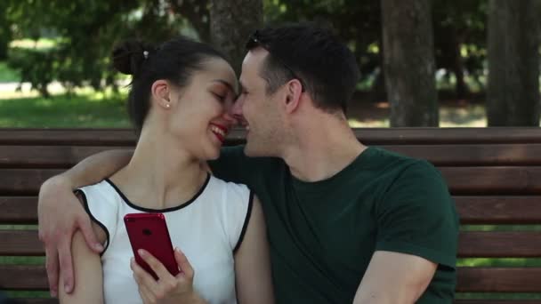 Young Lovers Laugh Kiss Bench Park Smiling Holding Smartphones Hands — Stock Video