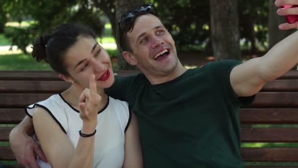 恋爱中的年轻夫妇 在阳光明媚的日子里 坐在公园的长椅上自拍自拍 他们面带微笑 互相拥抱 — 图库视频影像