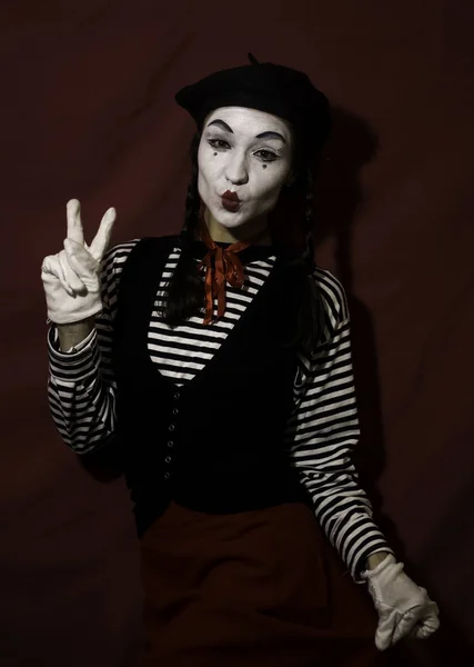 Beautiful mime girl grimaces and shows a victory sign with her hand.