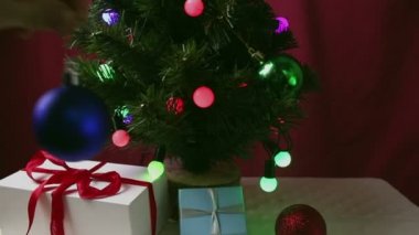 Genç bir kızın eli Noel ağacına mavi, parlak bir top asar. Çelengi ve parlak topları olan yeni yıl ağacı. Bir kız Noel ağacı süslüyor. Güzel paketlerdeki hediyeler Noel ağacının altında yatıyor.