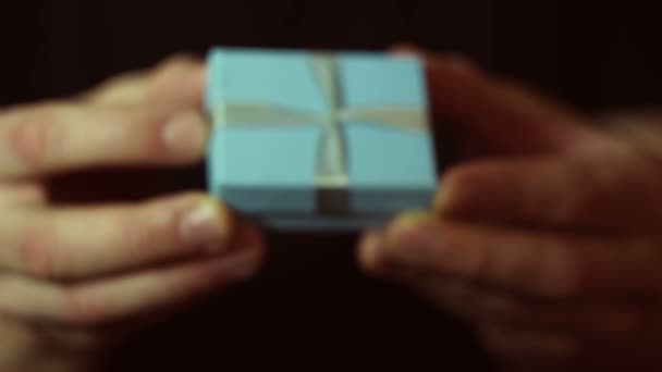 Muž drží dar v modré krabici. Ruce mladého muže podávají novoroční dárek v malé modré krabičce. Dárek na dovolenou.